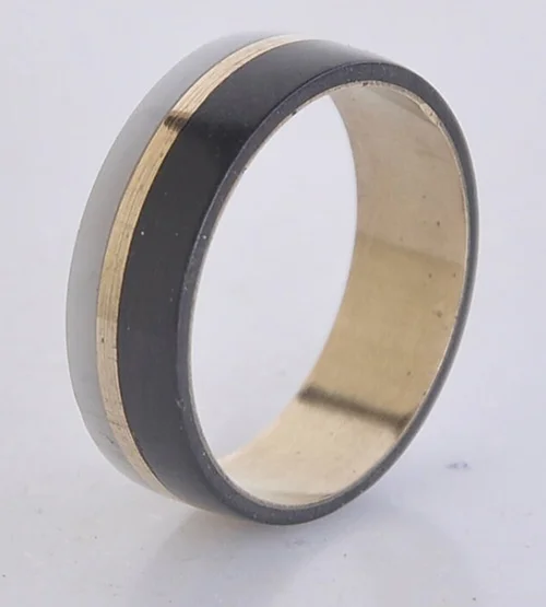 Unedited photo of a black and gold inlay men's band, with dust on the metal and a dull grey studio background