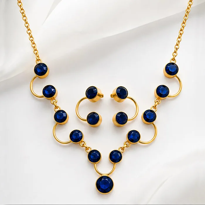 Gold-tone necklace and stud earring set with round blue stones, styled on soft white silk fabric