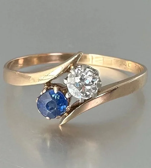 Ring retouching result: a gold two-stone bypass ring with blue and pink round stones on a white background